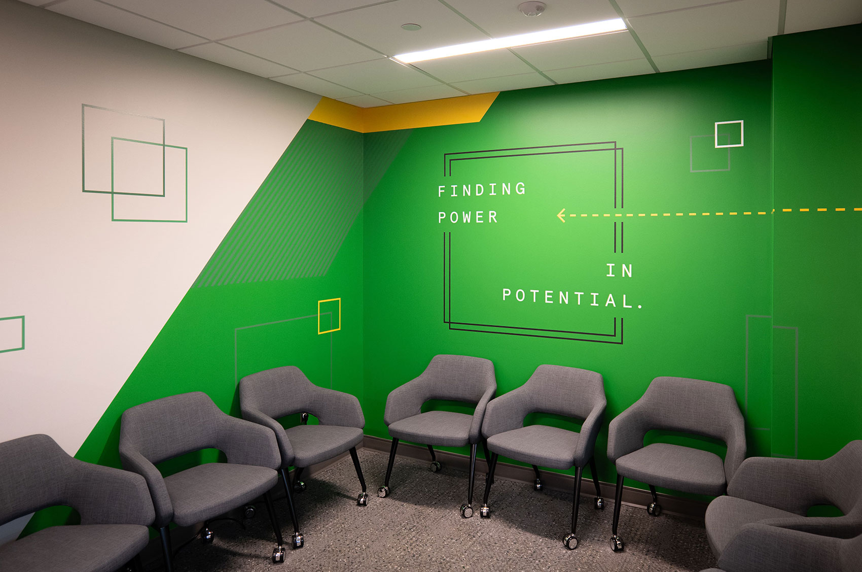 Modern conference room with gray chairs and green motivational wall art saying, Finding Power in Potential.