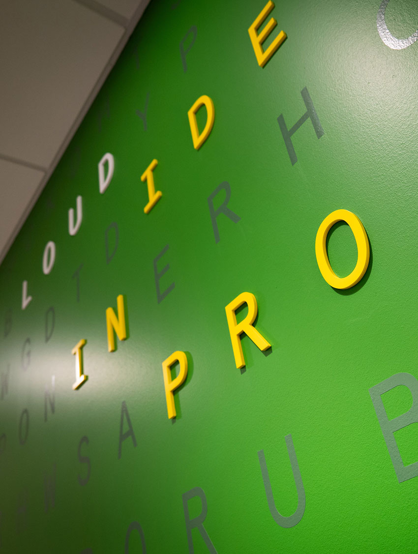 Green wall with protruding yellow letters forming words in a diagonal pattern, creating a dynamic visual effect.