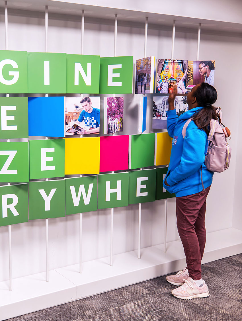 Person interacting with colorful educational wall display showcasing diverse images and inspiring messages.