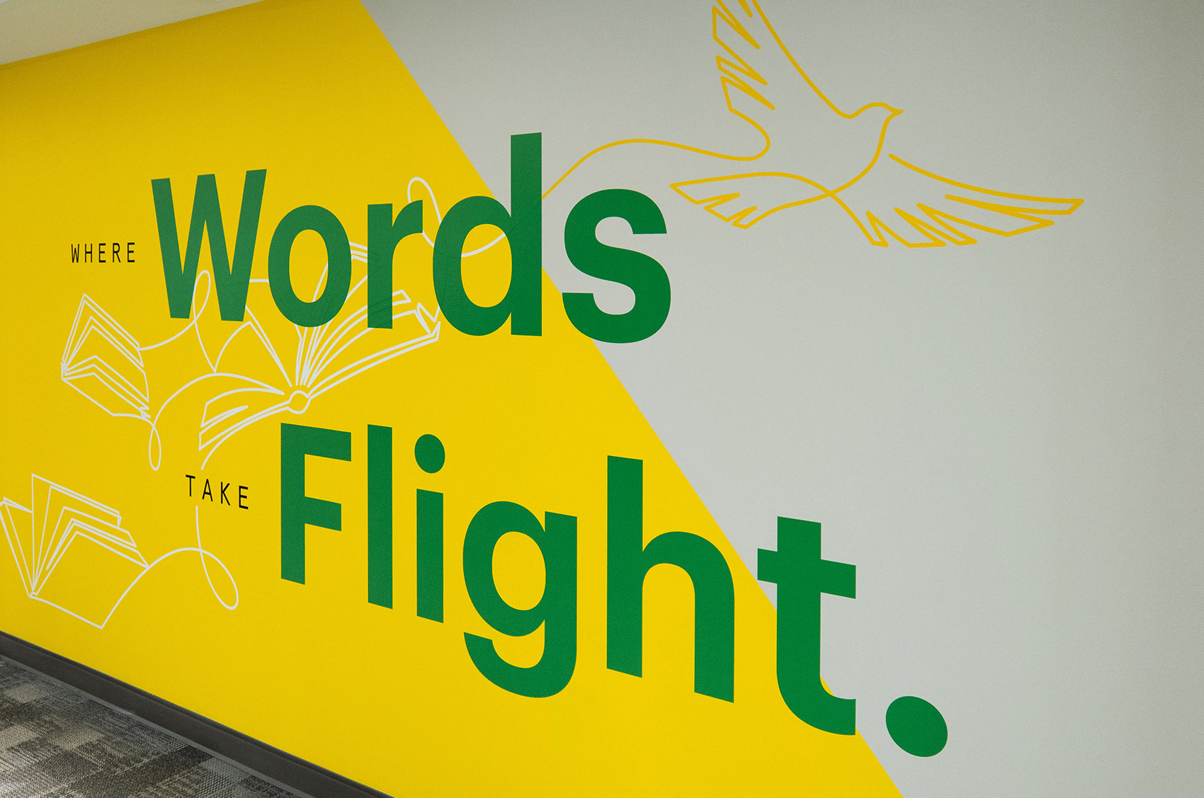 Wall mural with Where Words Take Flight in green on a yellow and gray background with bird and book graphics.