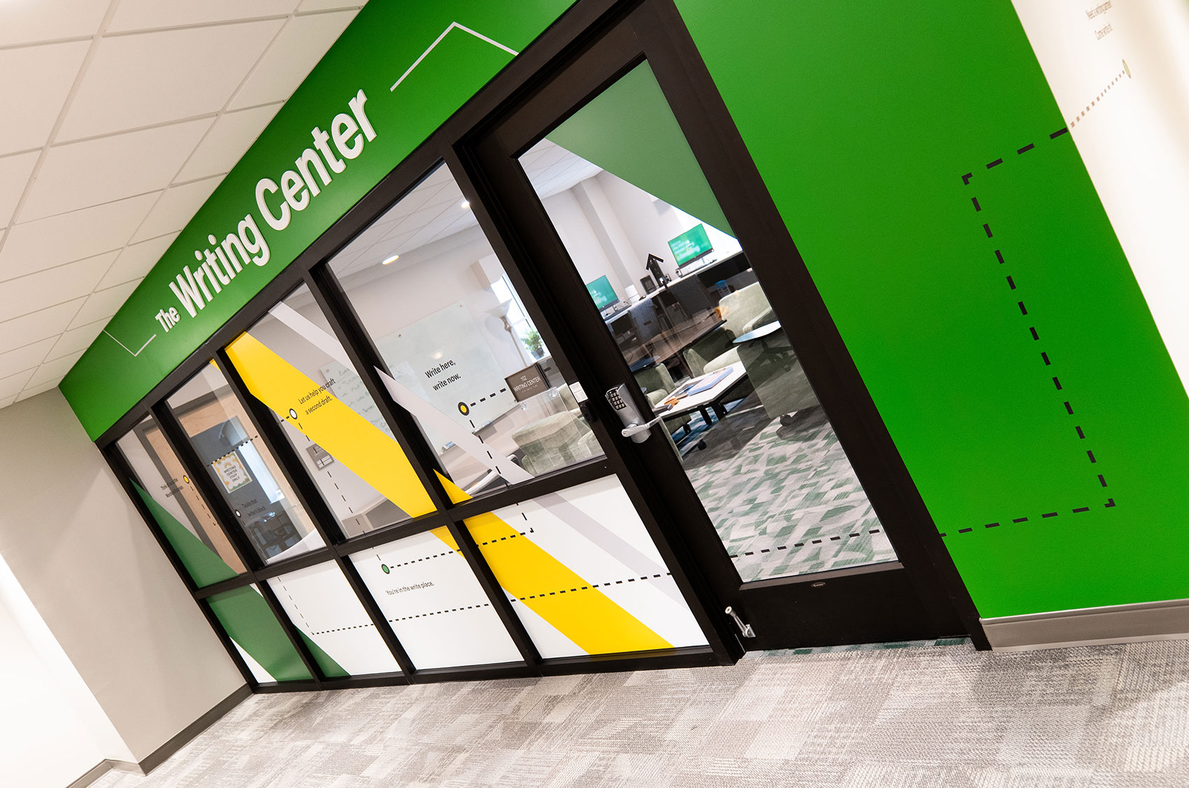 Writing Center entrance with green and yellow decor, glass walls, and modern interior workspace visible.